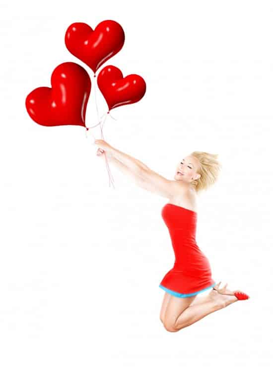 Happy girl flying, holding red heart balloons
