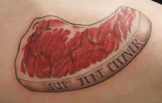 A tattoo of a slab of meat which says “RIP June Cleaver” on it