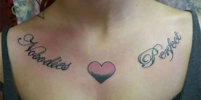 A tattoo on a woman’s chest which says “Nobodies perfect” with a heart in the middle 