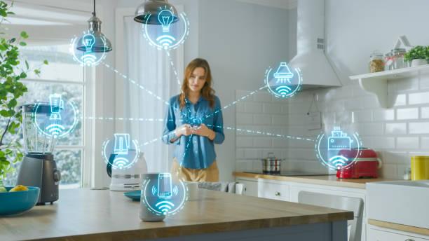 Internet of Things Concept: Young Woman Using Smartphone in Kitchen. She controls her Kitchen Appliances with IOT. Graphics Showing Digitalization Visualization of Connected Home Electronics Devices Internet of Things Concept: Young Woman Using Smartphone in Kitchen. She controls her Kitchen Appliances with IOT. Graphics Showing Digitalization Visualization of Connected Home Electronics Devices IoT devices stock pictures, royalty-free photos & images